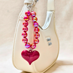 Pink beaded keychain with a heart charm attached to a beige handbag.