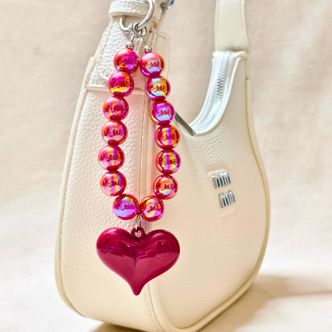 Pink beaded keychain with a heart charm attached to a beige handbag.
