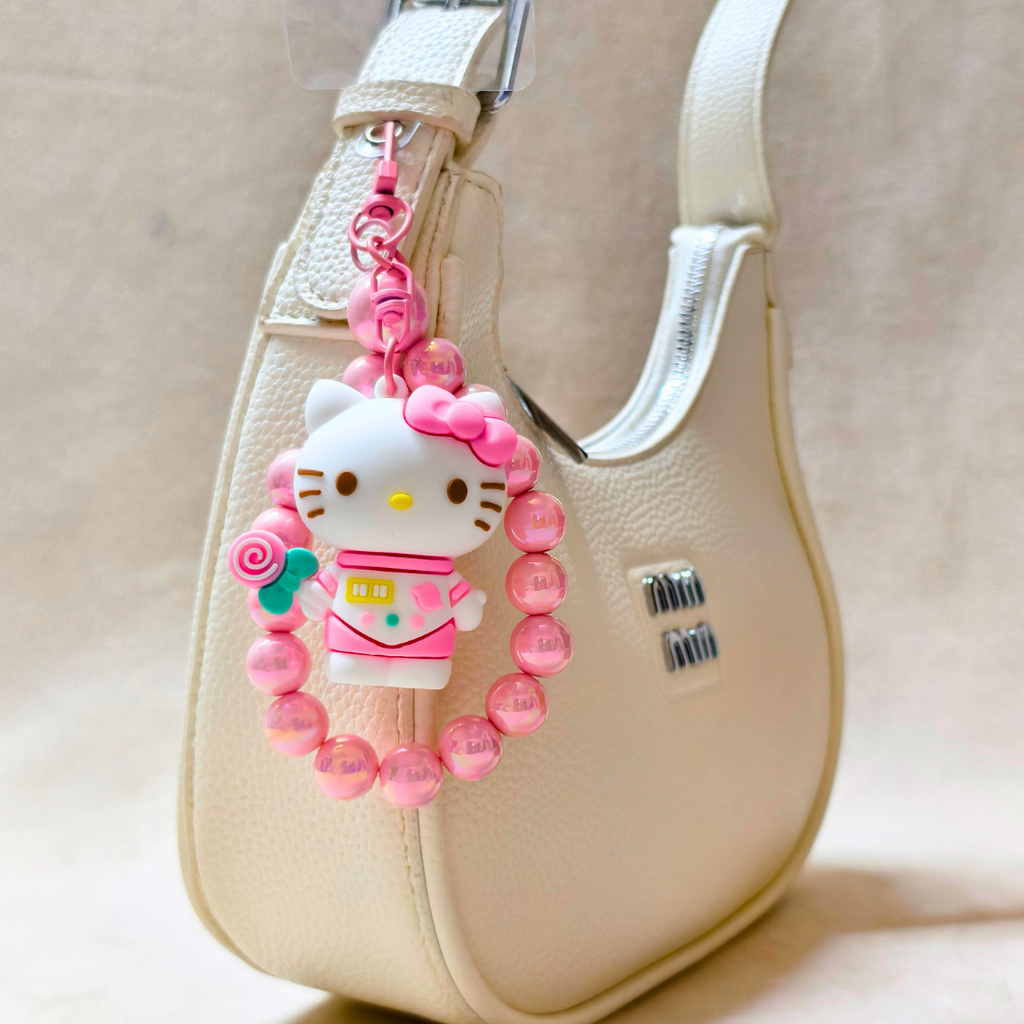 Pink Hello Kitty keychain attached to a beige handbag.