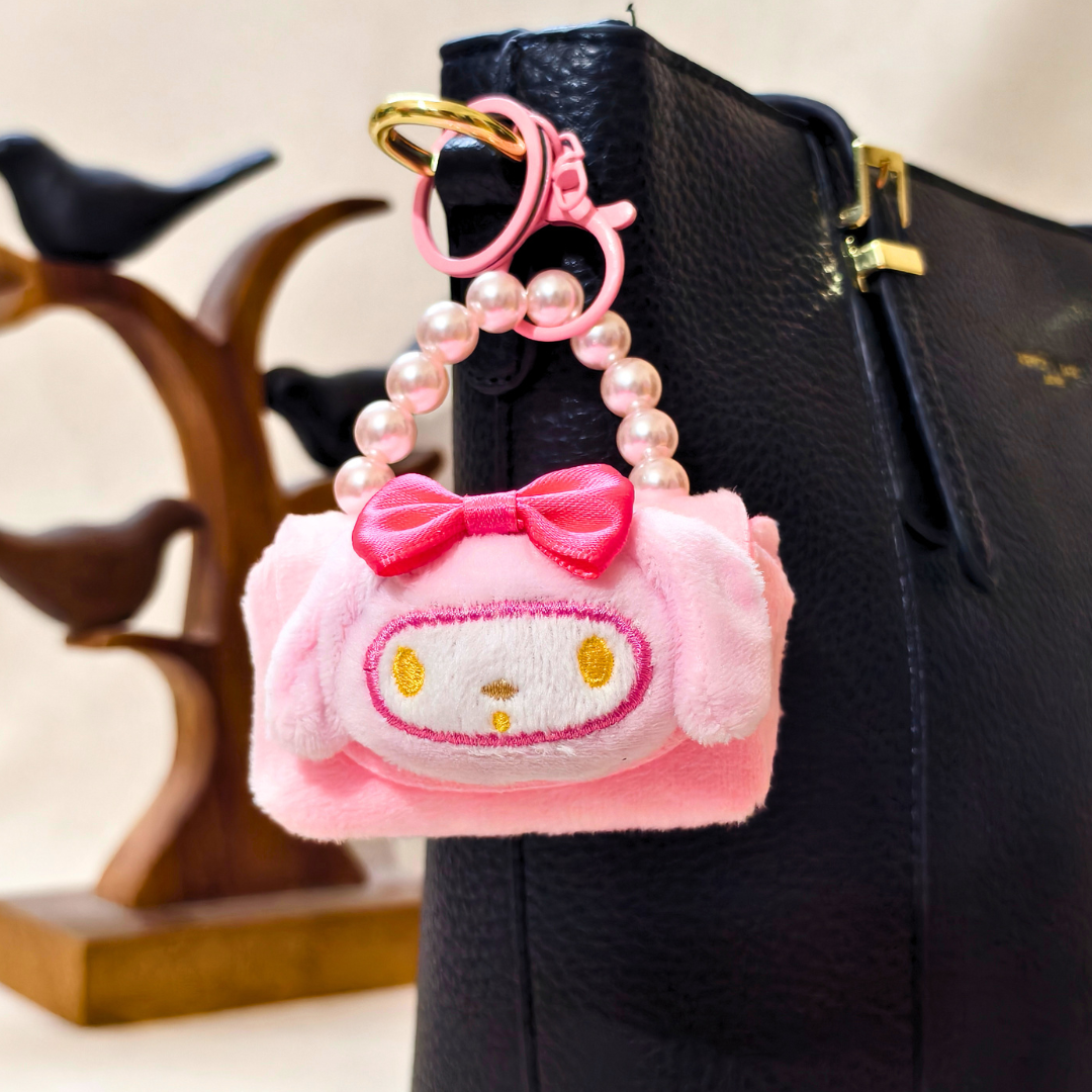 Pink plush keychain with a bow attached to a black bag.