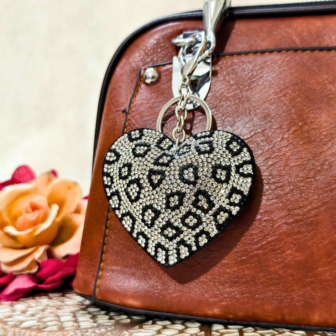 Heart-shaped keychain with leopard print pattern attached to a brown leather bag.