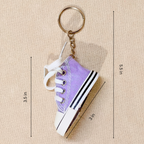 A miniature purple canvas high-top sneaker keychain with white laces, a white rubber toe cap, and black stripes, shown with dimension lines and measurements on a beige textured background.