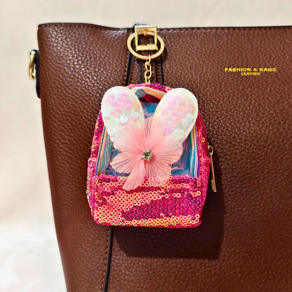 Pink sequined backpack charm with butterfly design on a brown leather bag.