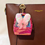 Pink sequined backpack charm with butterfly design on a brown leather bag.