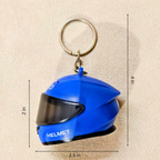 A blue racing helmet keychain with a silver metal key ring, shown on a beige textured background with dimension lines indicating measurements of 2.5 in width, 4 in height, and 2 in depth.