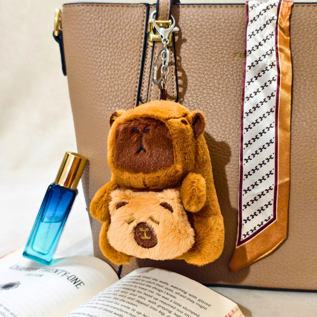 Two teddy bear keychains on a beige handbag with a blue perfume bottle and open book in the foreground.