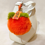Orange fluffy keychain with green accents attached to a white handbag.