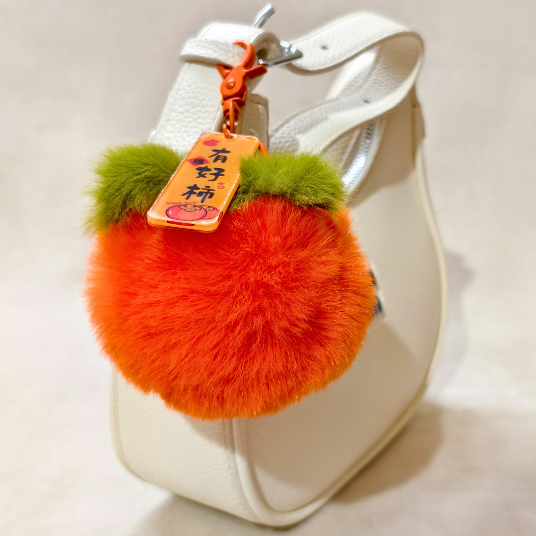 Orange fluffy keychain with green accents attached to a white handbag.
