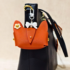 Orange cat-shaped pouch with decorative elements attached to a black handbag.