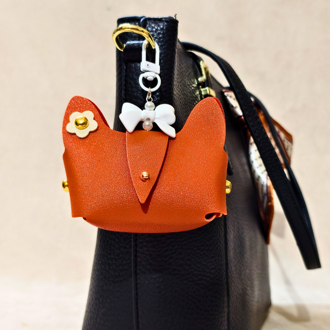 Orange cat-shaped pouch with decorative elements attached to a black handbag.