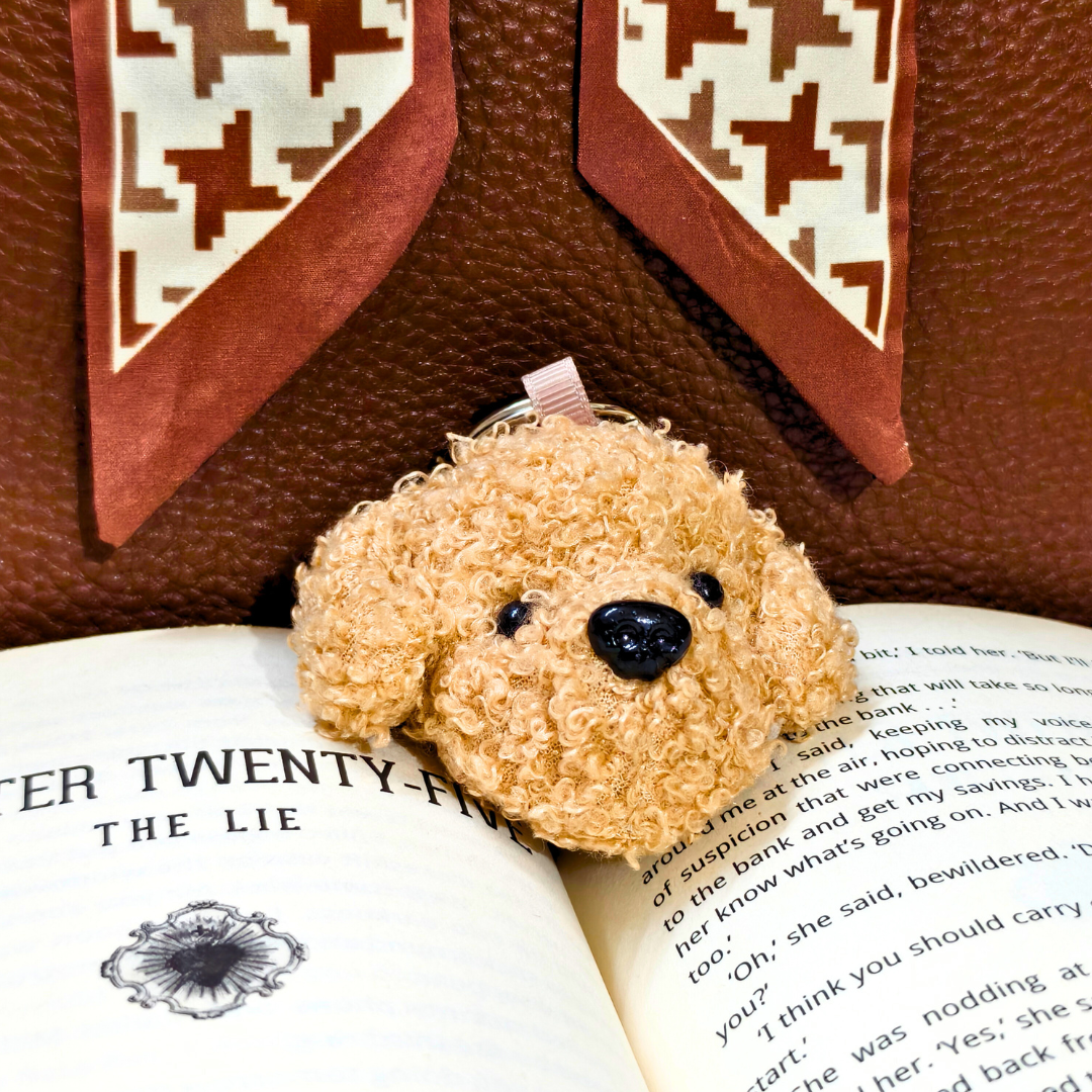 Small brown teddy bear keychain on an open book with a patterned fabric background
