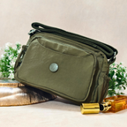Military Green Sling Bag With Props In Front Of Beige Background.