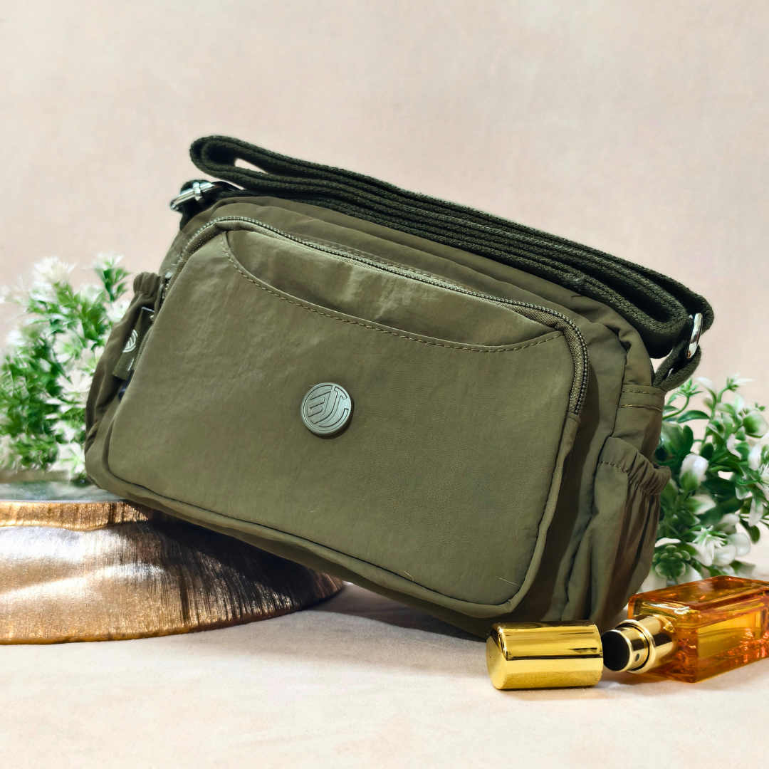 Military Green Sling Bag With Props In Front Of Beige Background.