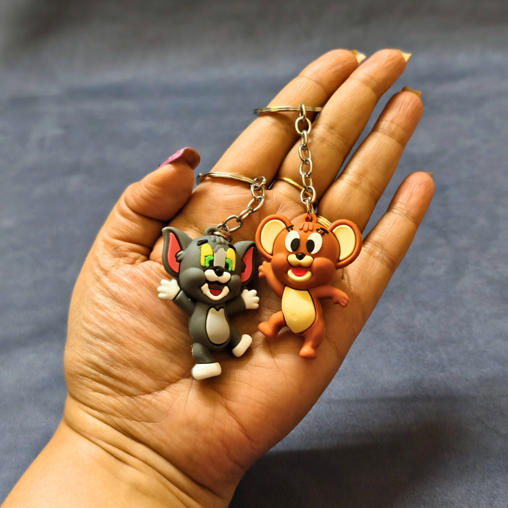 Hand holding two cartoon character keychains against a dark background