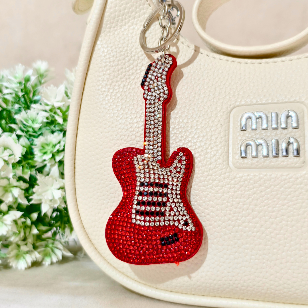 Red Guitar Bag Charm Attached On Purse In The Front Of Beige Background.