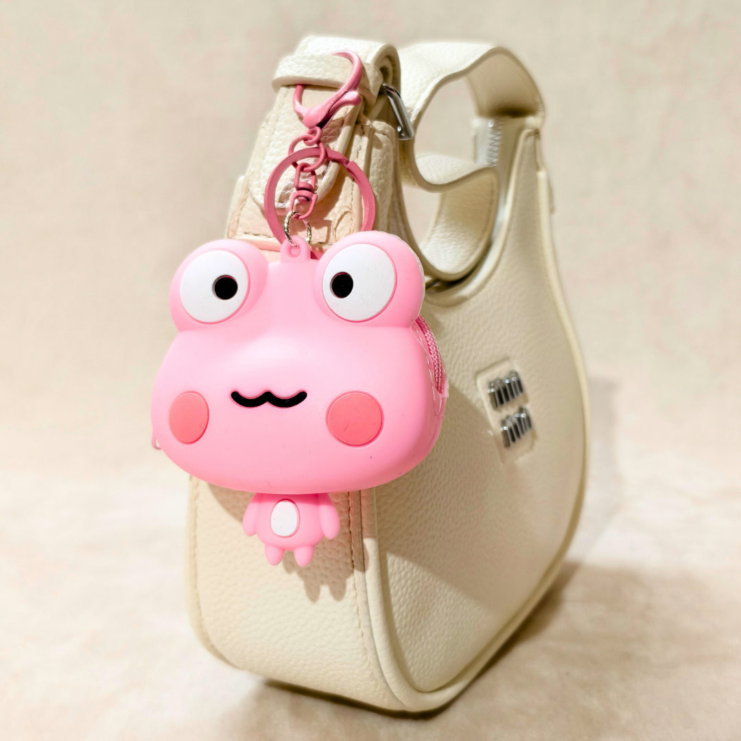 Pink cartoon frog keychain attached to a beige bag on a beige background