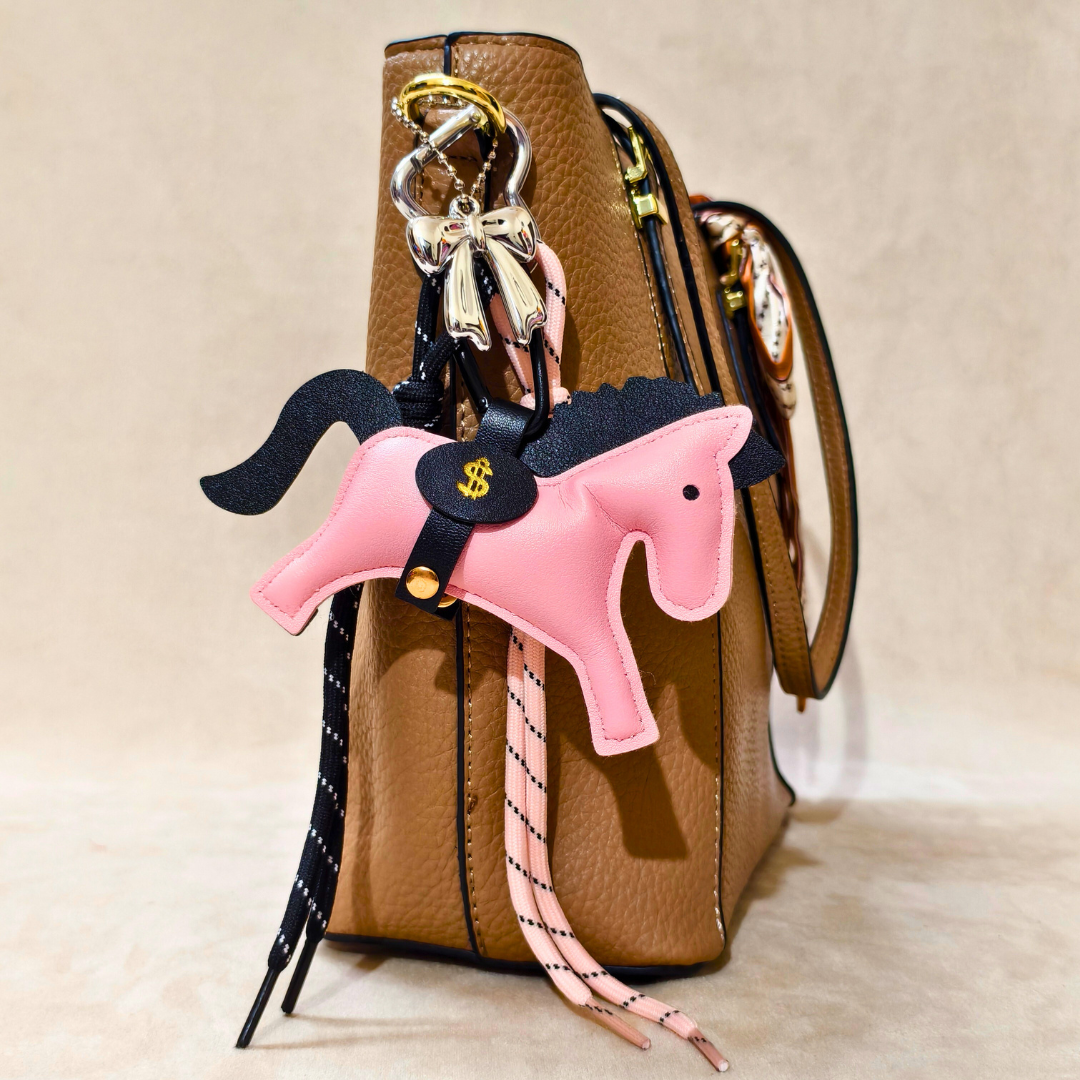 Pink horse-shaped keychain with a black strap attached to a brown handbag.