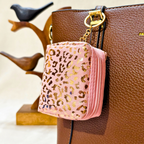 Pink leopard print pouch attached to a brown handbag with decorative elements.
