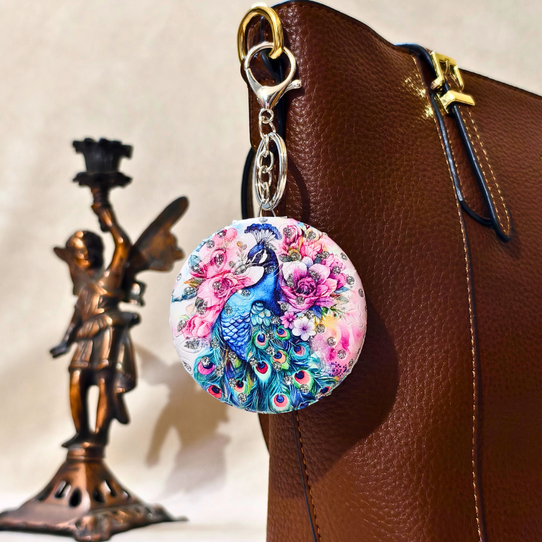 Keychain with peacock design attached to a brown leather bag