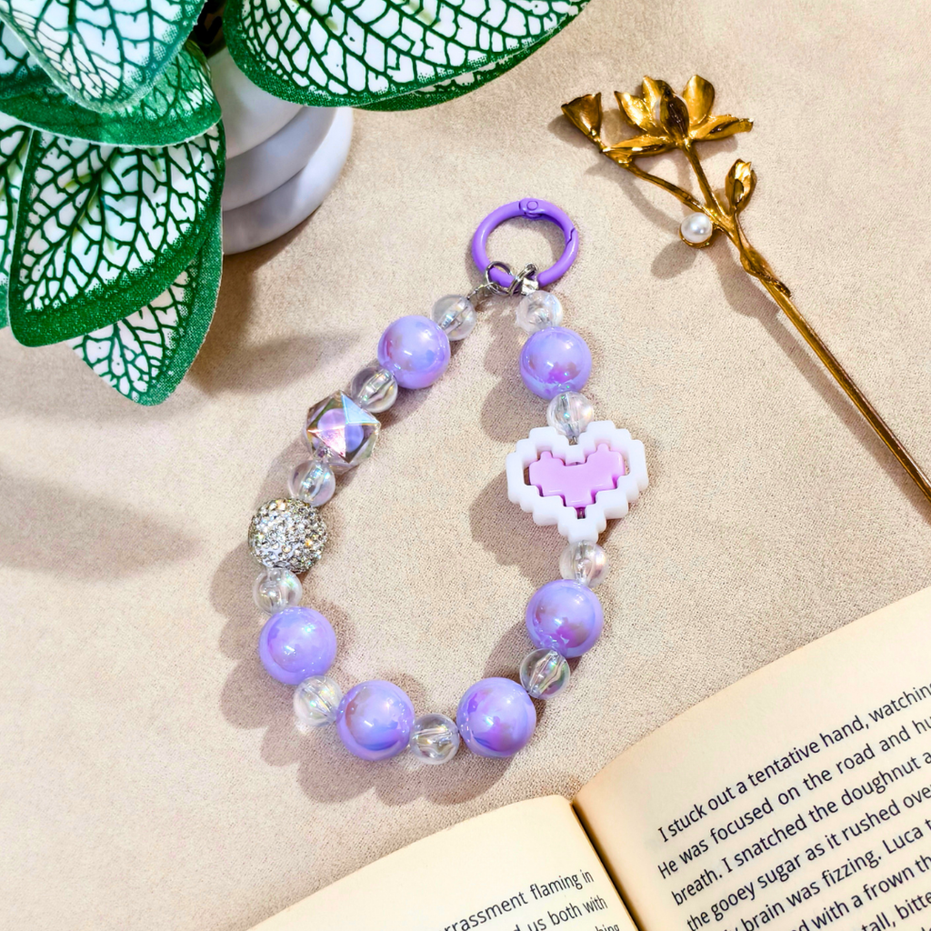 Purple beaded bracelet with a heart charm on an open book with decorative elements.