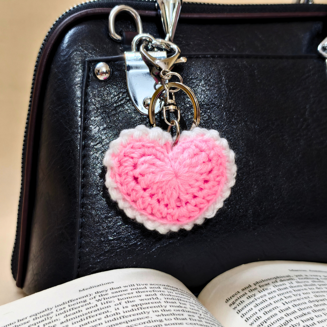 Pink heart-shaped keychain on a black leather bag with an open book underneath