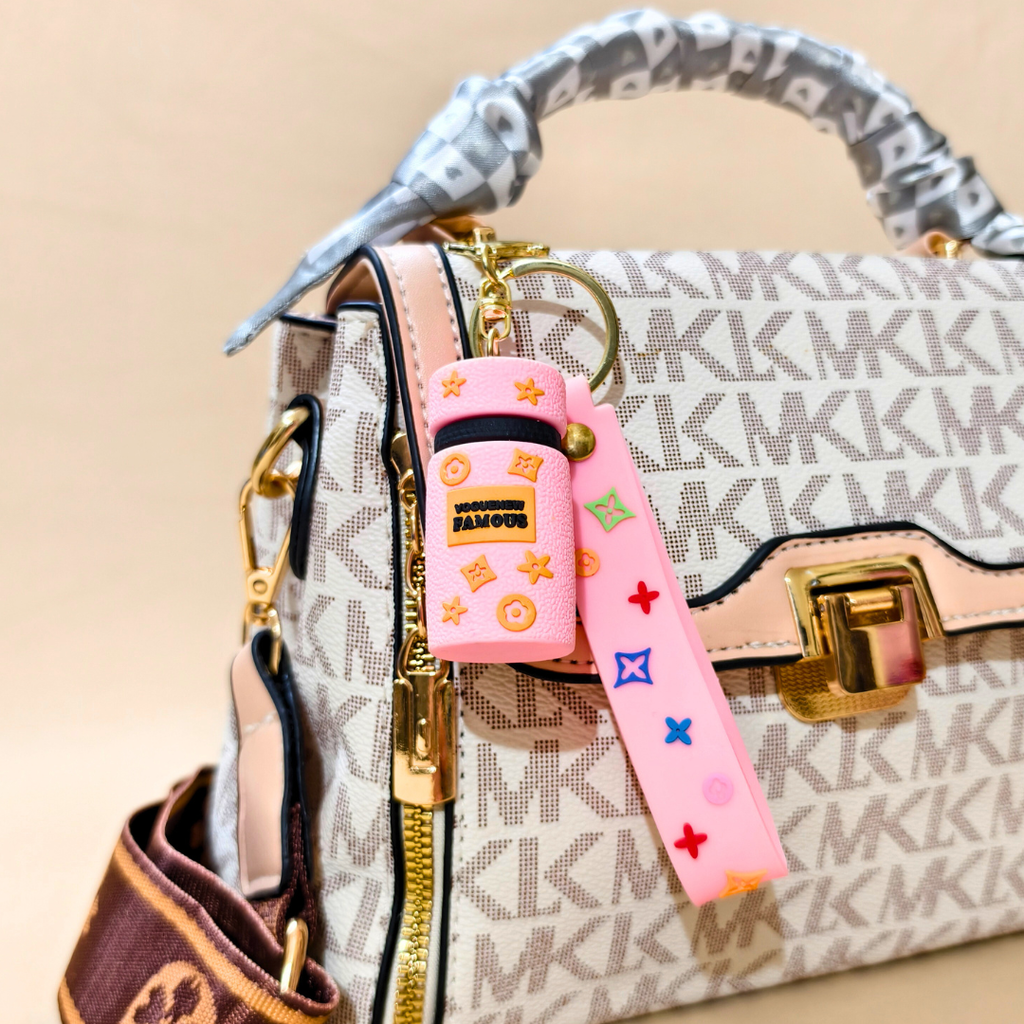 Designer handbag with a pink keychain featuring colorful designs on a beige background