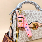 Designer handbag with a pink keychain featuring colorful designs on a beige background