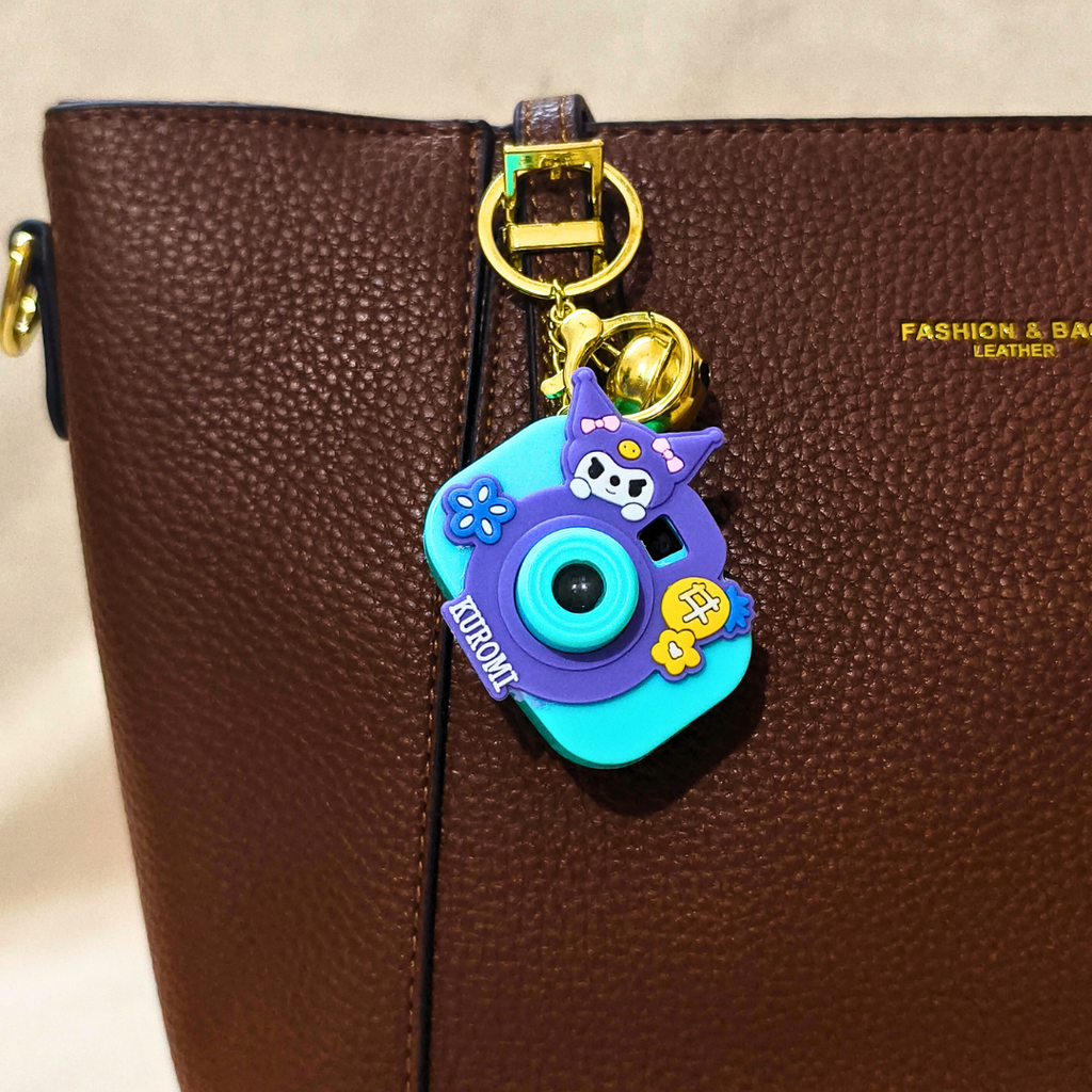 Colorful keychain shaped like a camera attached to a brown leather bag.