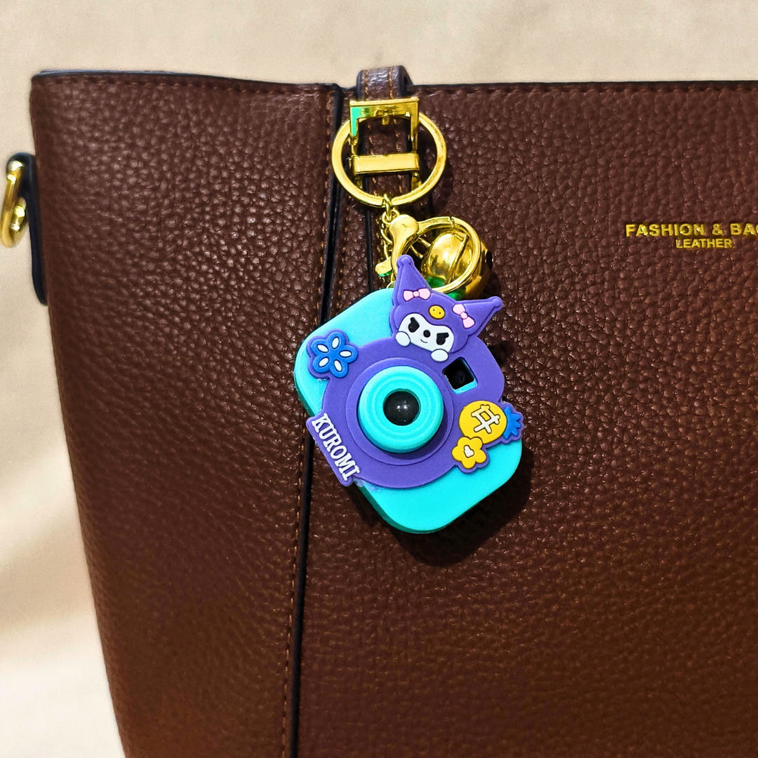 Colorful keychain shaped like a camera attached to a brown leather bag.