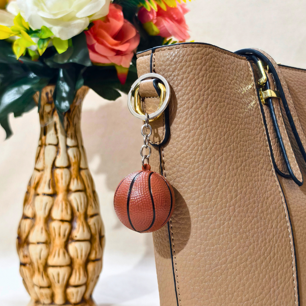 A miniature basketball-shaped keychain attached on a Tan Handbag as Bag Charm against a plain beige background.