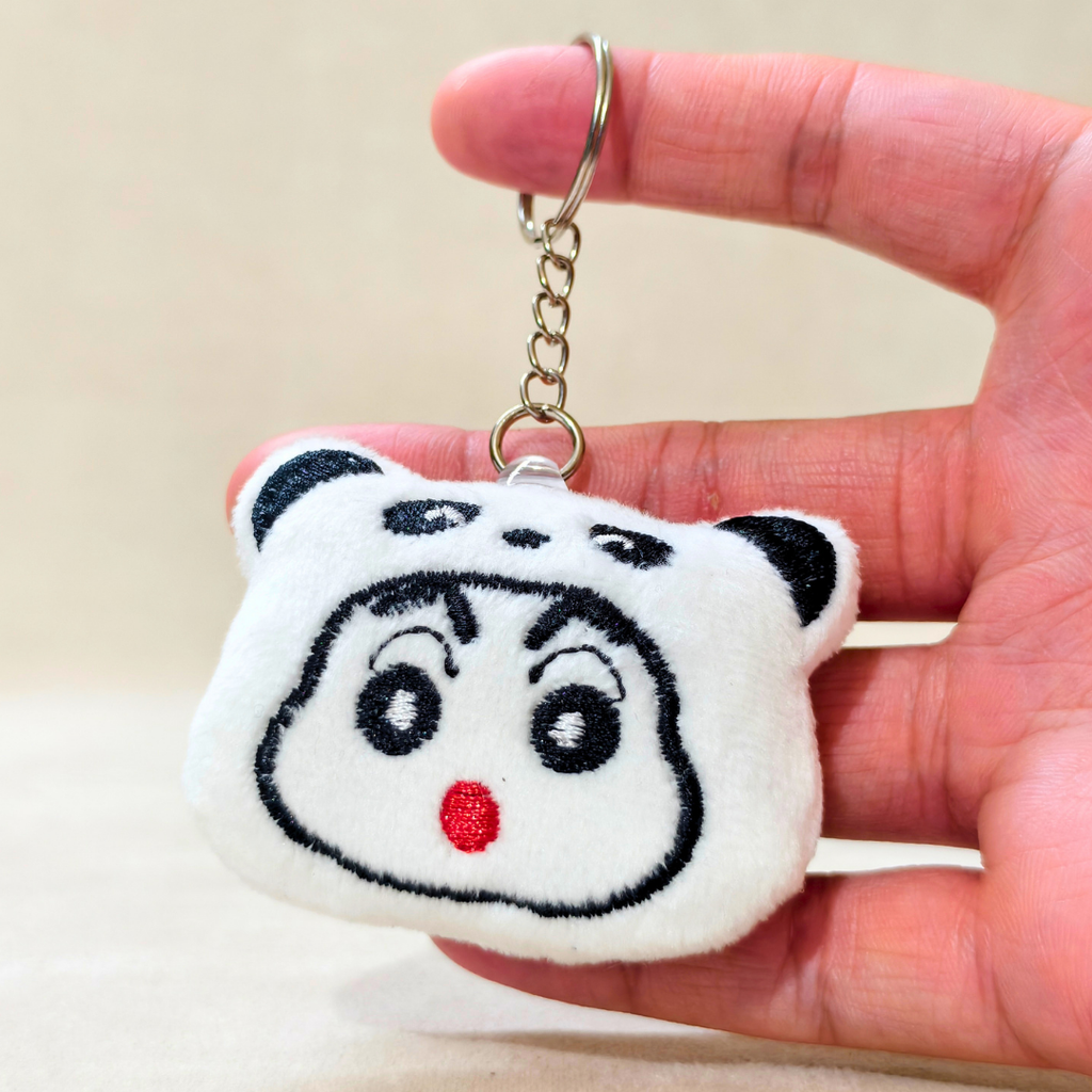 A plush white bear-shaped keychain with embroidered black facial features and a small red nose, attached to a silver metal key ring, held in a person's hand against a soft beige background.