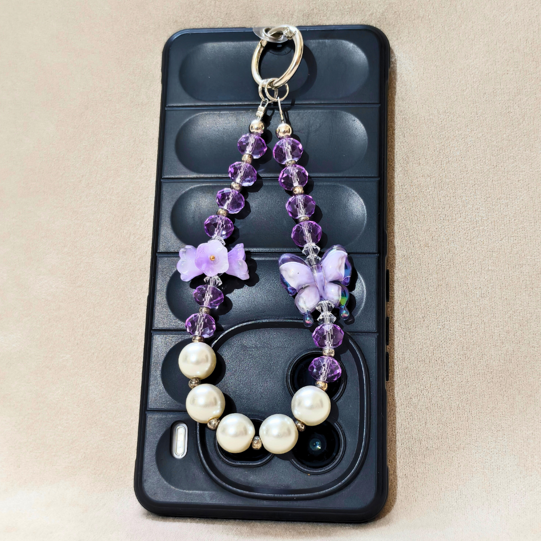 Phone case with a decorative keychain featuring purple flowers and pearls on a beige background