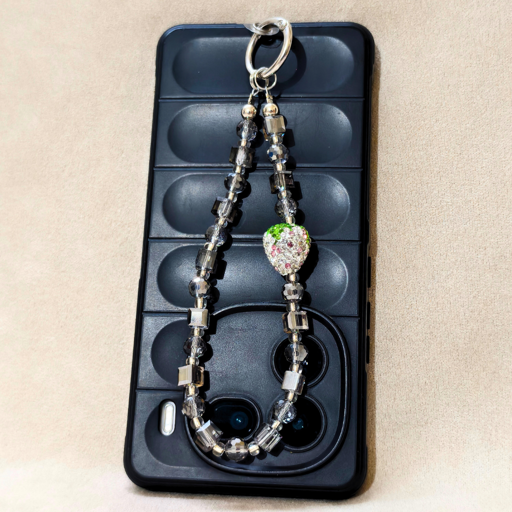 Decorative keychain with beads on a black phone case against a beige background
