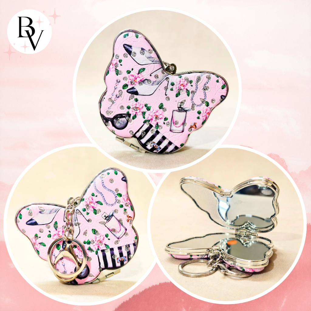 A butterfly-shaped compact mirror keychain shown in three views: closed with floral pink pattern and key ring, closed with butterfly wings open, and open showing a mirror. The background is a soft pink gradient with a 'BV' logo in the top left.