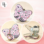 A butterfly-shaped compact mirror keychain shown in three views: closed with floral pink pattern and key ring, closed with butterfly wings open, and open showing a mirror. The background is a soft pink gradient with a 'BV' logo in the top left.