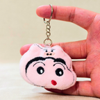 A plush keychain shaped like a cartoon pig face, featuring embroidered black eyebrows, eyes, and mouth details, a small red stitched nose, and a gold metal key ring and chain shown hand carry On Beige Background.