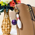 Sporty Bowling Keychain along with Silver chain and ring with Ball attached on Tan Color Handbag as Bag  charm on Beige Background.