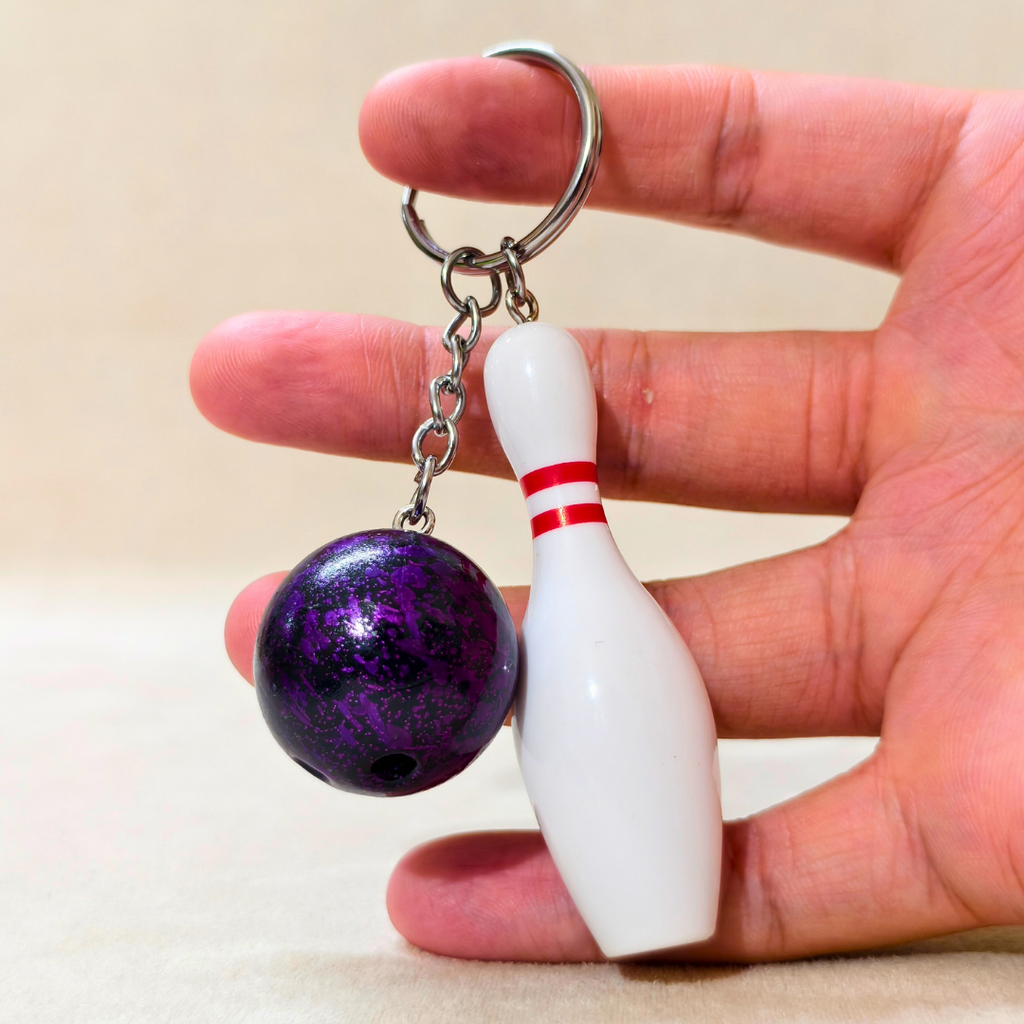 Sporty Bowling Keychain along with Silver chain and ring with Ball hold in hand  on Beige Background.