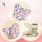 A butterfly-shaped compact mirror keychain shown in three views: closed with a lipstick-patterned wing and keychain ring, closed with the wing folded, and open showing a butterfly-shaped mirror. The wing pattern features lipstick tubes and red lips on a white background.