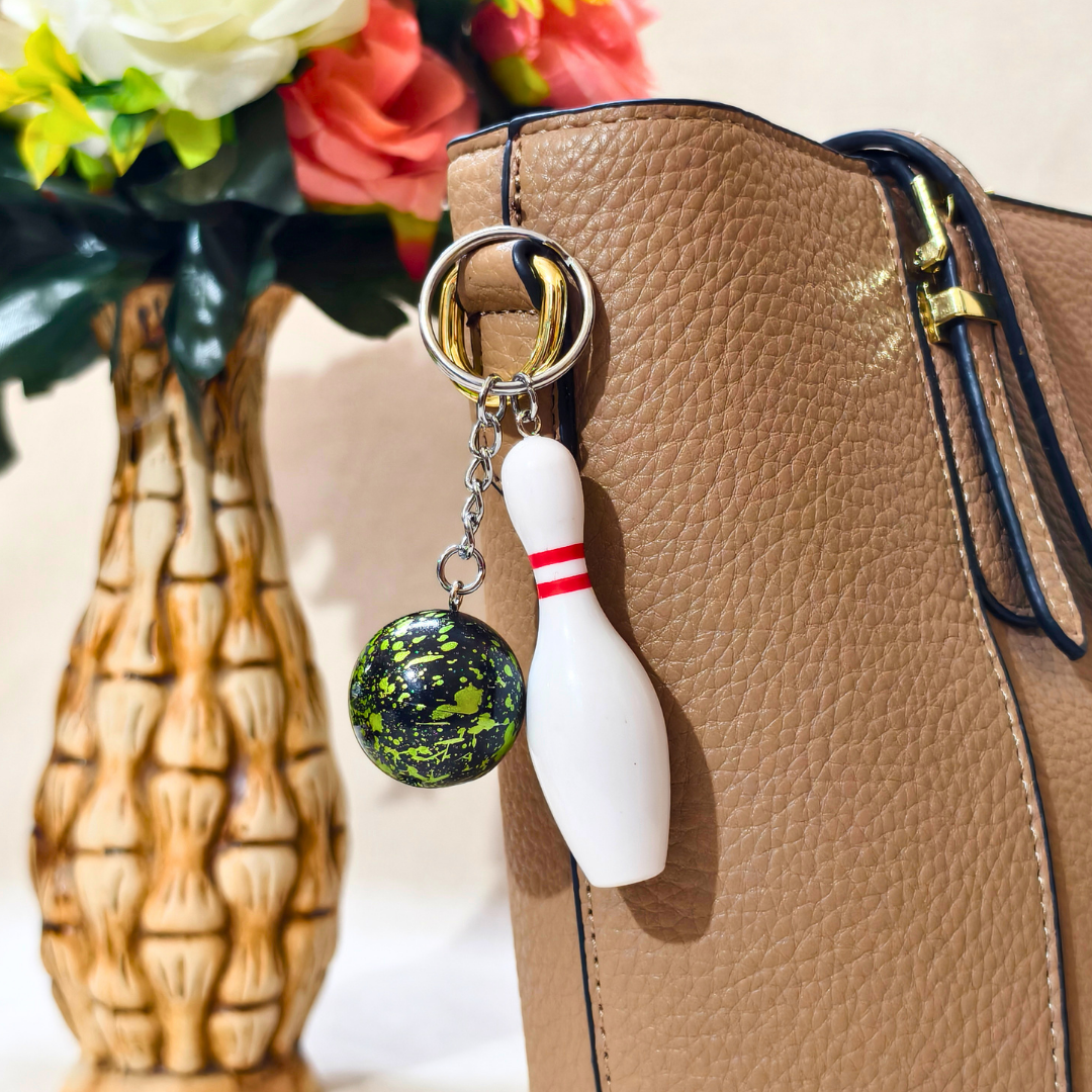 Sporty Keychain showing Bowling Bottle Along with silver chain and ring with Ball attached on Tan Handbag as Bag charm on Beige background. 