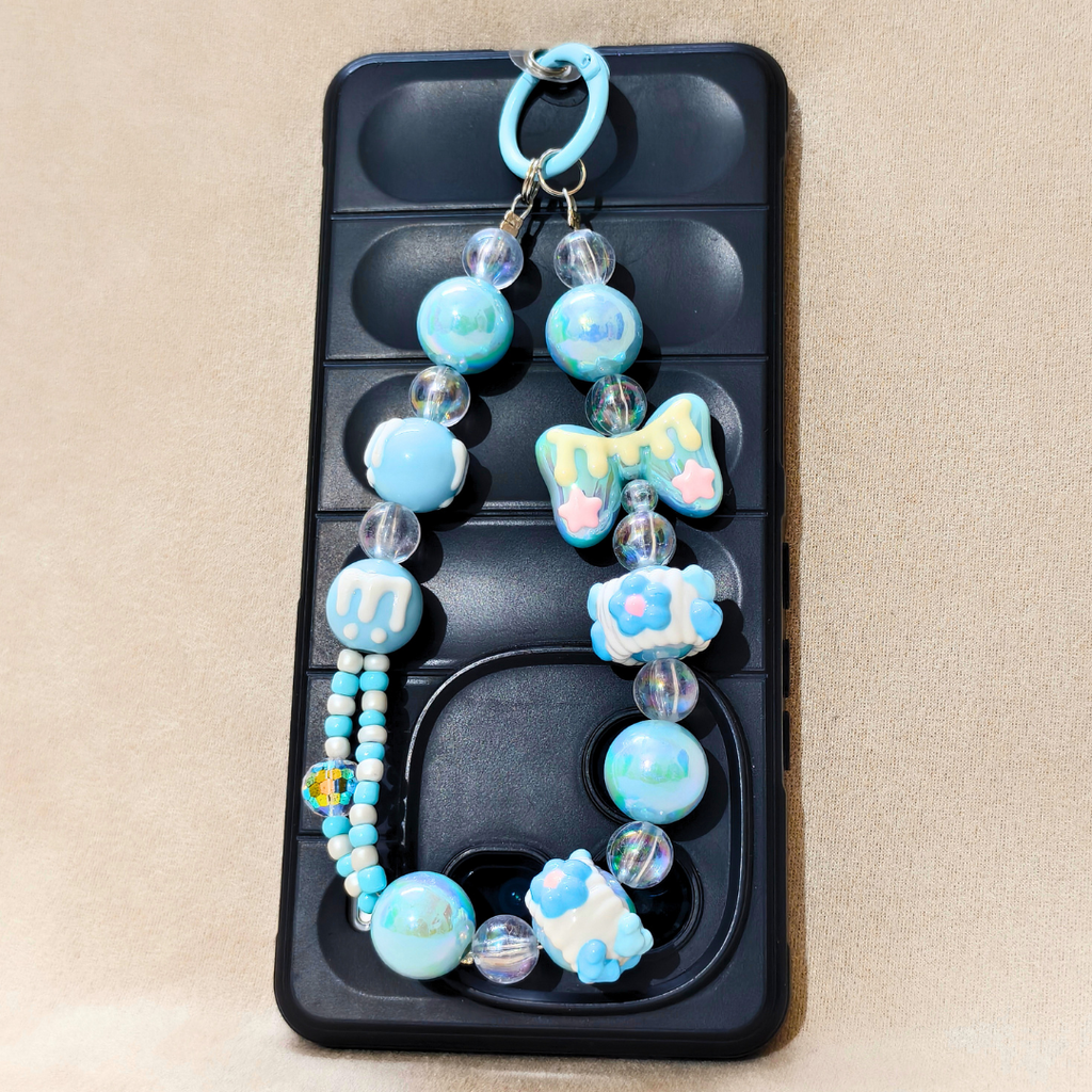 Decorative phone charm with blue and white beads and charms on a phone case.