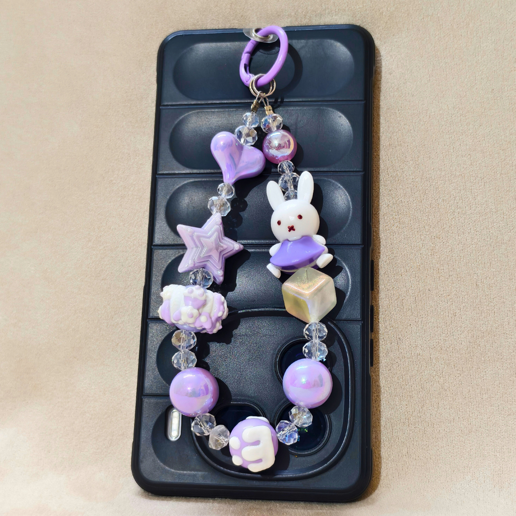 Decorative phone charm with a rabbit figure, stars, and hearts on a black phone case.