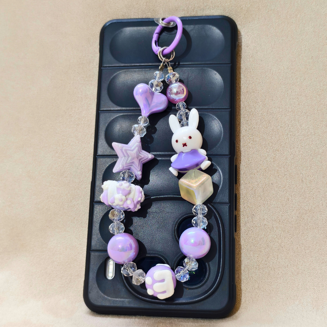 Decorative phone charm with a rabbit figure, stars, and hearts on a black phone case.