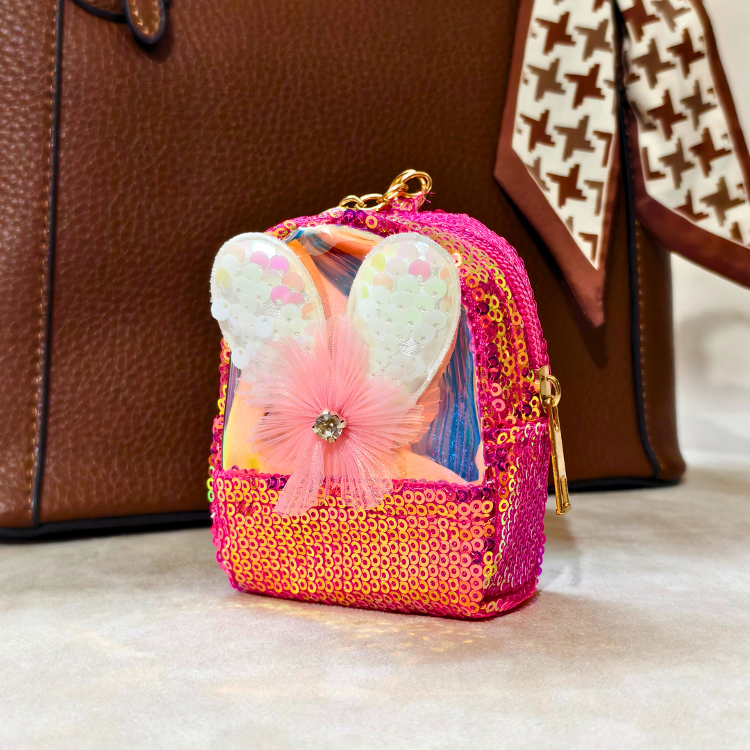 Pink and gold butterfly keychain in a clear bag with a brown leather bag and patterned fabric in the background.