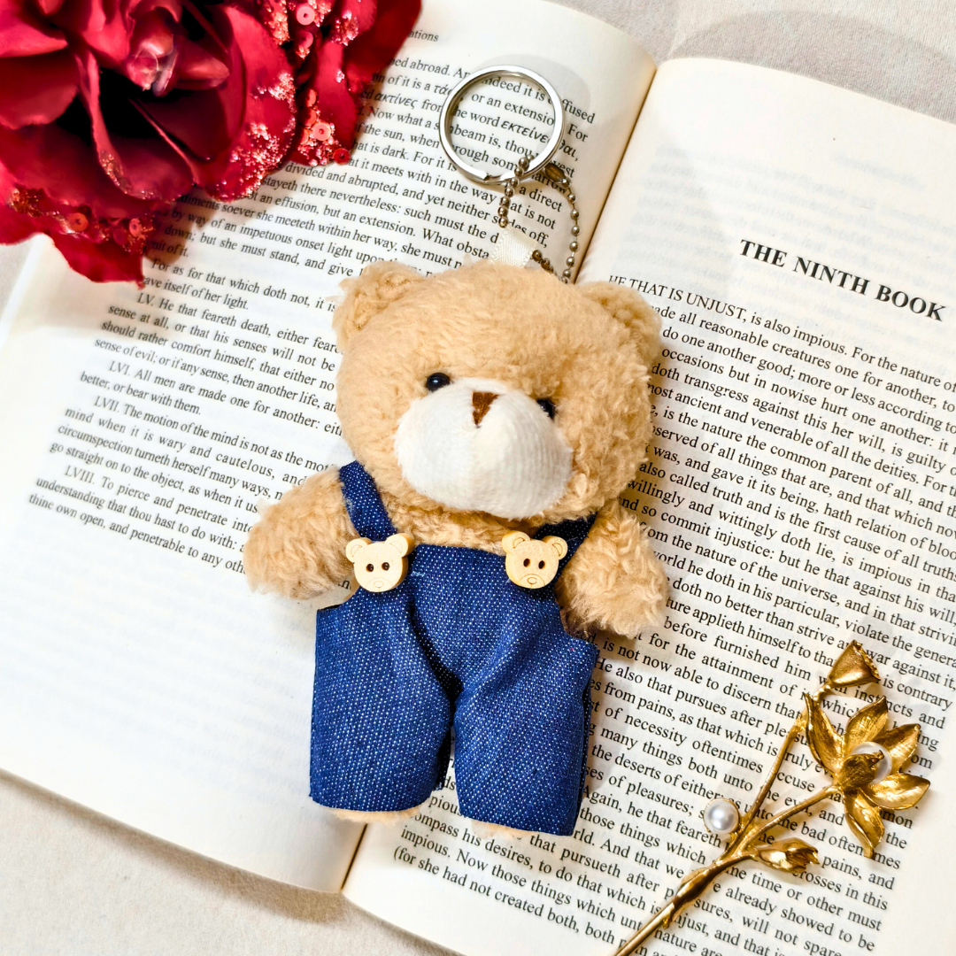 Small teddy bear with blue overalls on an open book with red flowers.