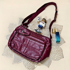 Maroon leather handbag on a decorative doily with small figurine and perfume bottle.