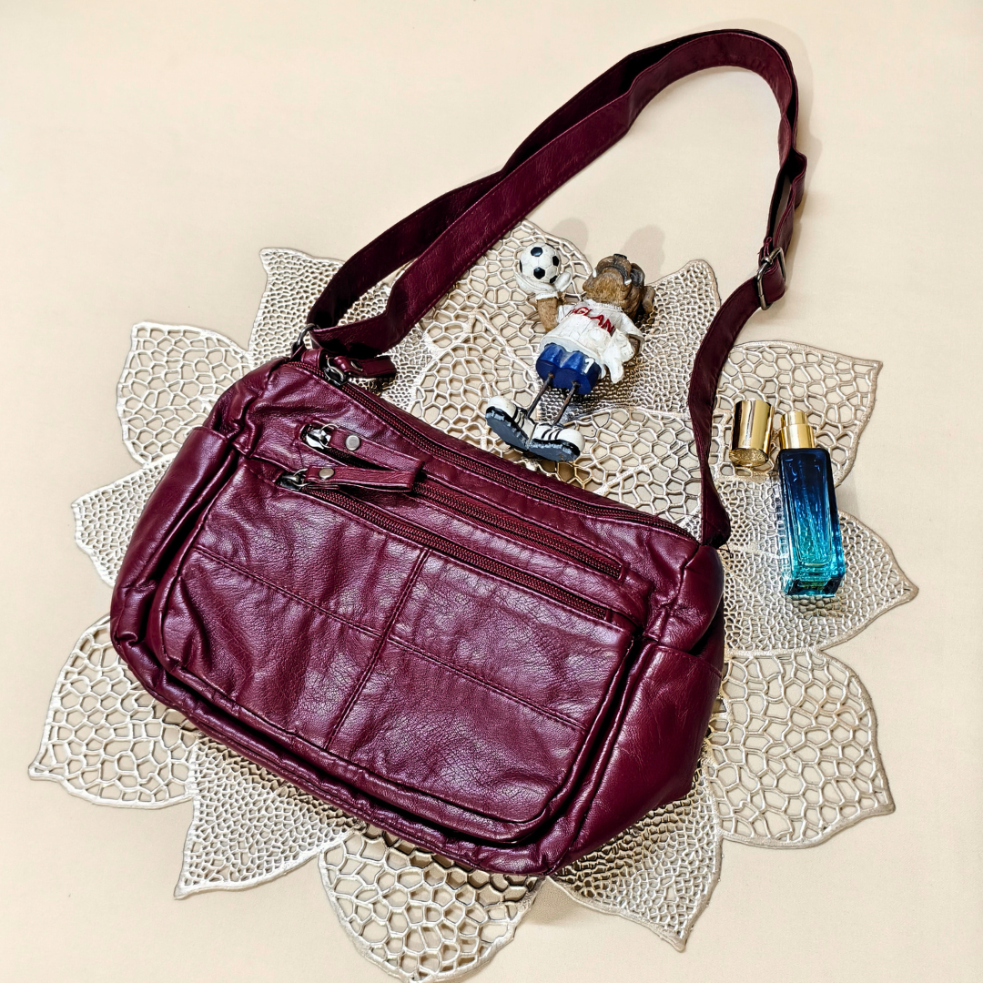 Maroon leather handbag on a decorative doily with small figurine and perfume bottle.