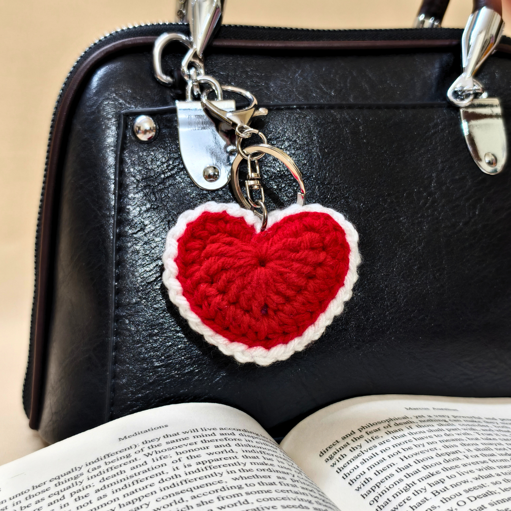 Red heart-shaped keychain on a black leather bag with an open book underneath.