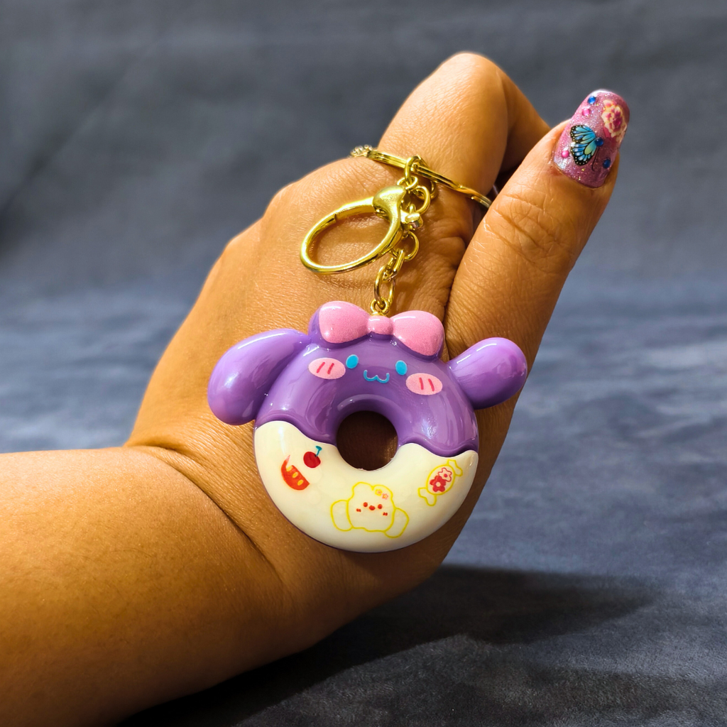 Hand holding a purple and pink donut-shaped keychain against a dark background
