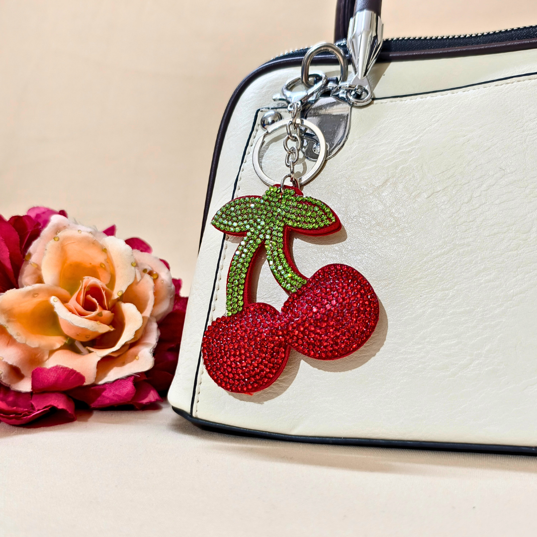 Cherry keychain with a metal latch placed on a purse beside a flower decoration in front of a beige background